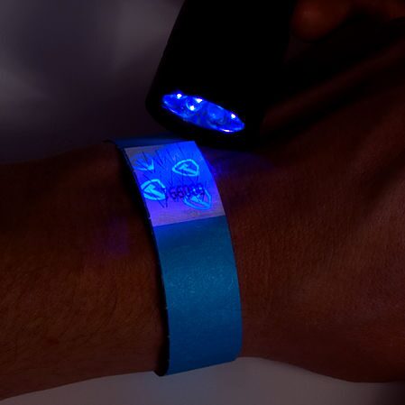 Una pulsera puesta en el antebrazo, iluminada con una linterna de luz negra: los símbolos de seguridad brillan en azul